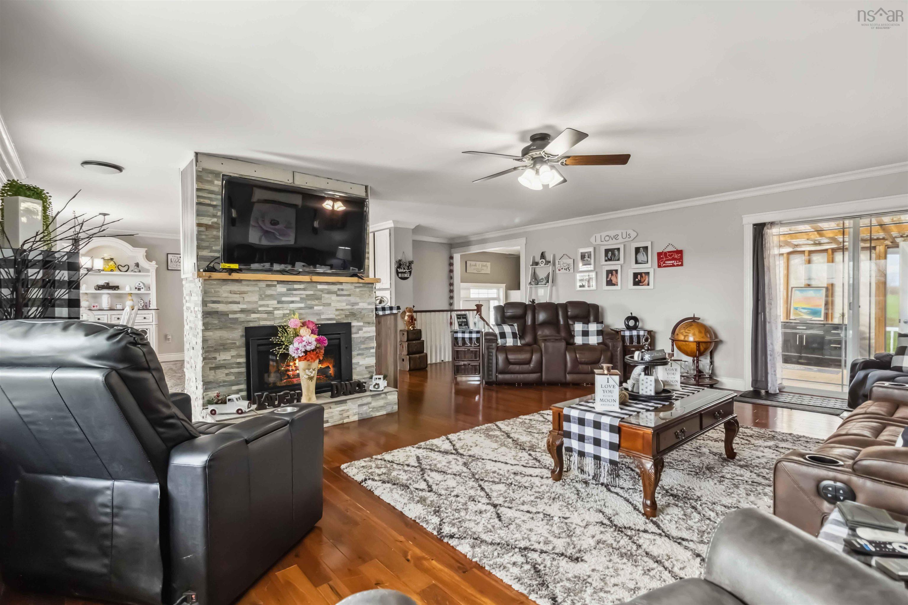 Living room featuring crown molding, ceiling fan, a stone fireplace, and wood finished floors