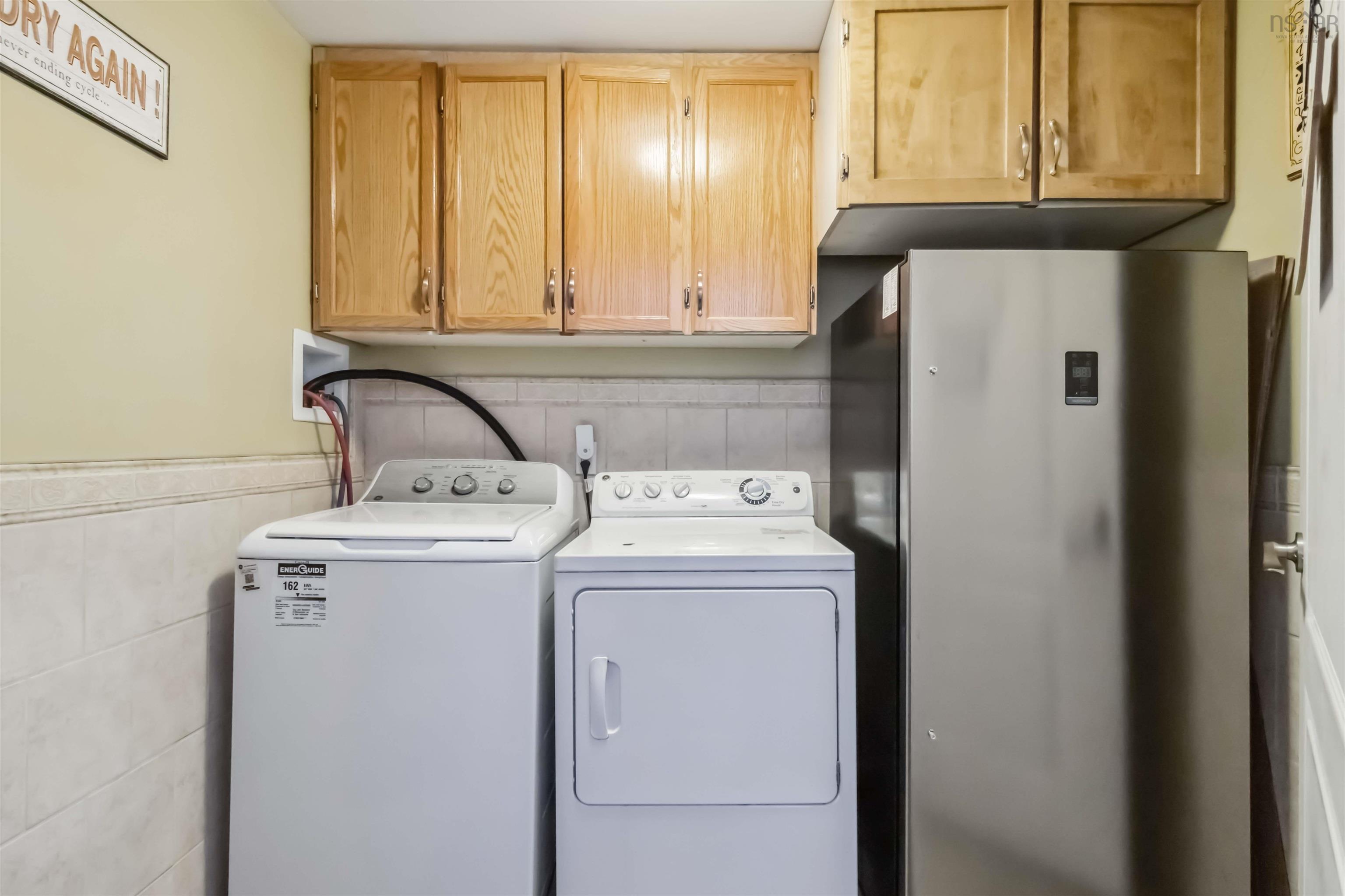 Laundry area with independent washer and dryer, cabinet space, tile walls, and a wainscoted wall
