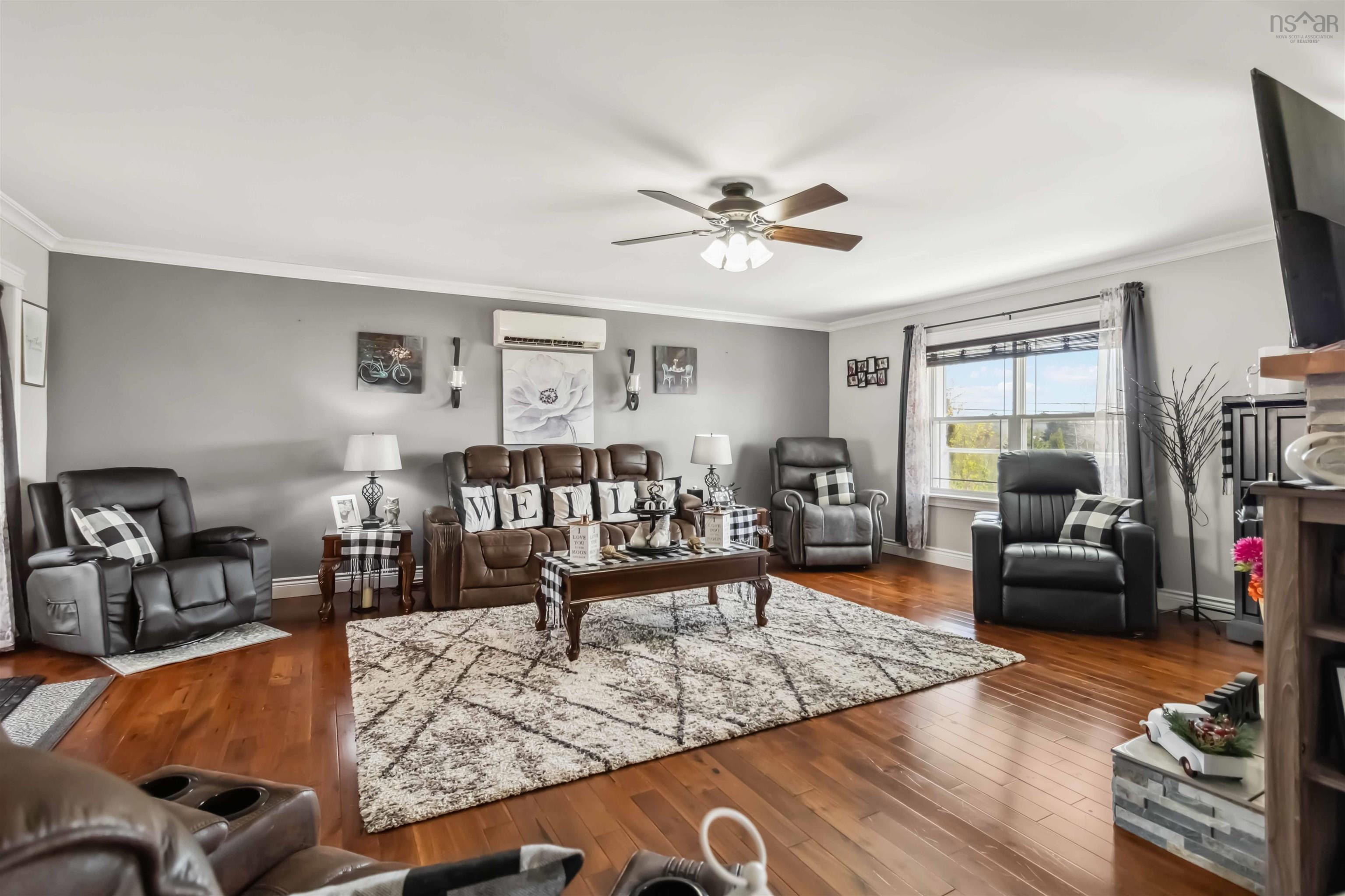 Living area with ceiling fan, ornamental molding, an AC wall unit, wood finished floors, and baseboards