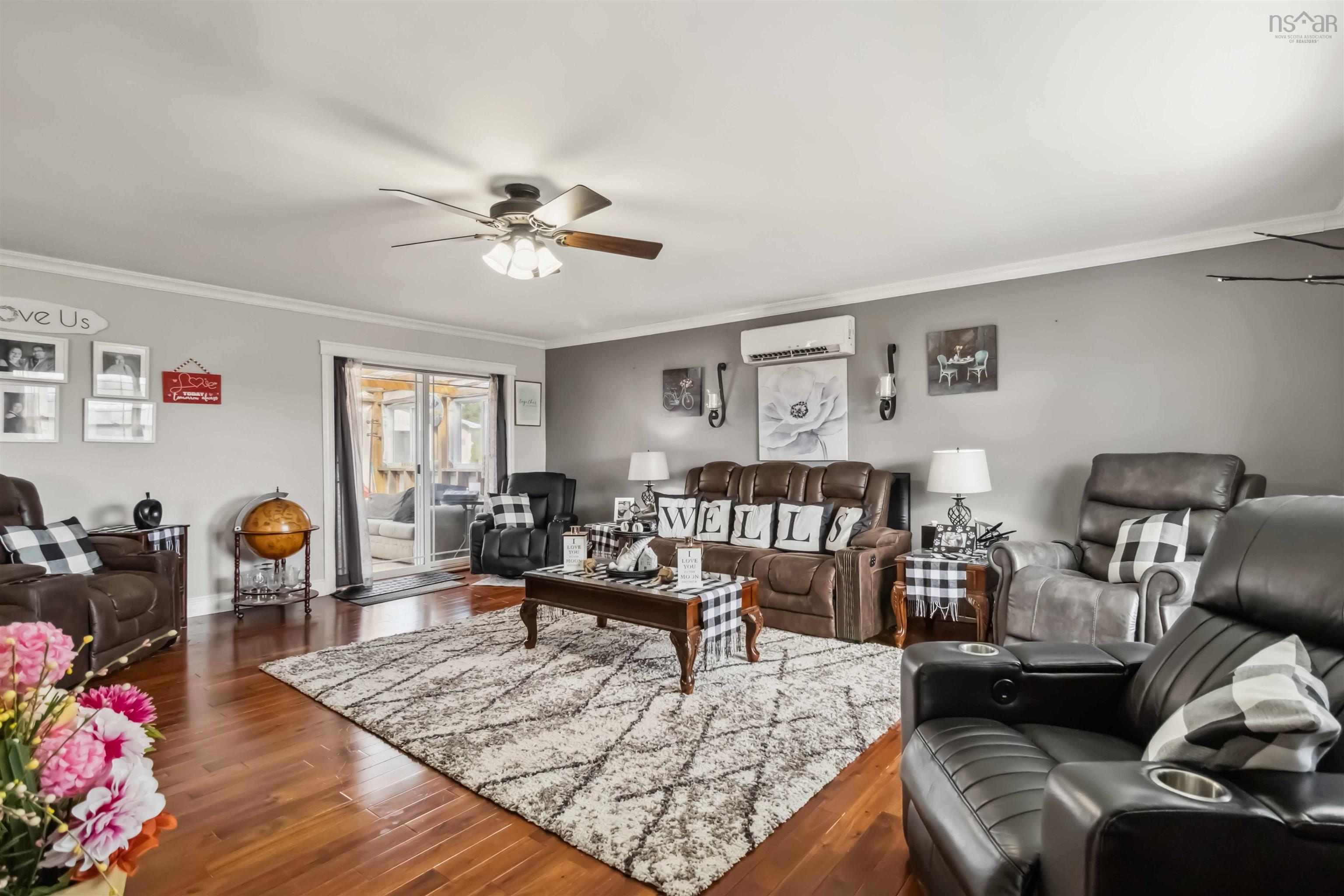 Living area with a wall unit AC, ceiling fan, crown molding, dark wood finished floors, and baseboards