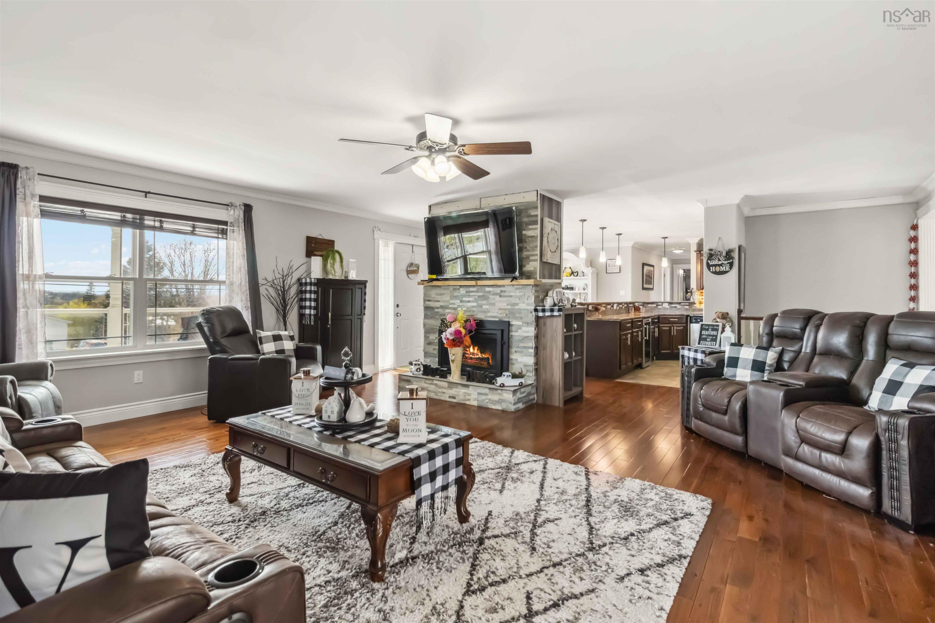 Living room with crown molding, a ceiling fan, a stone fireplace, dark wood-type flooring, and baseboards