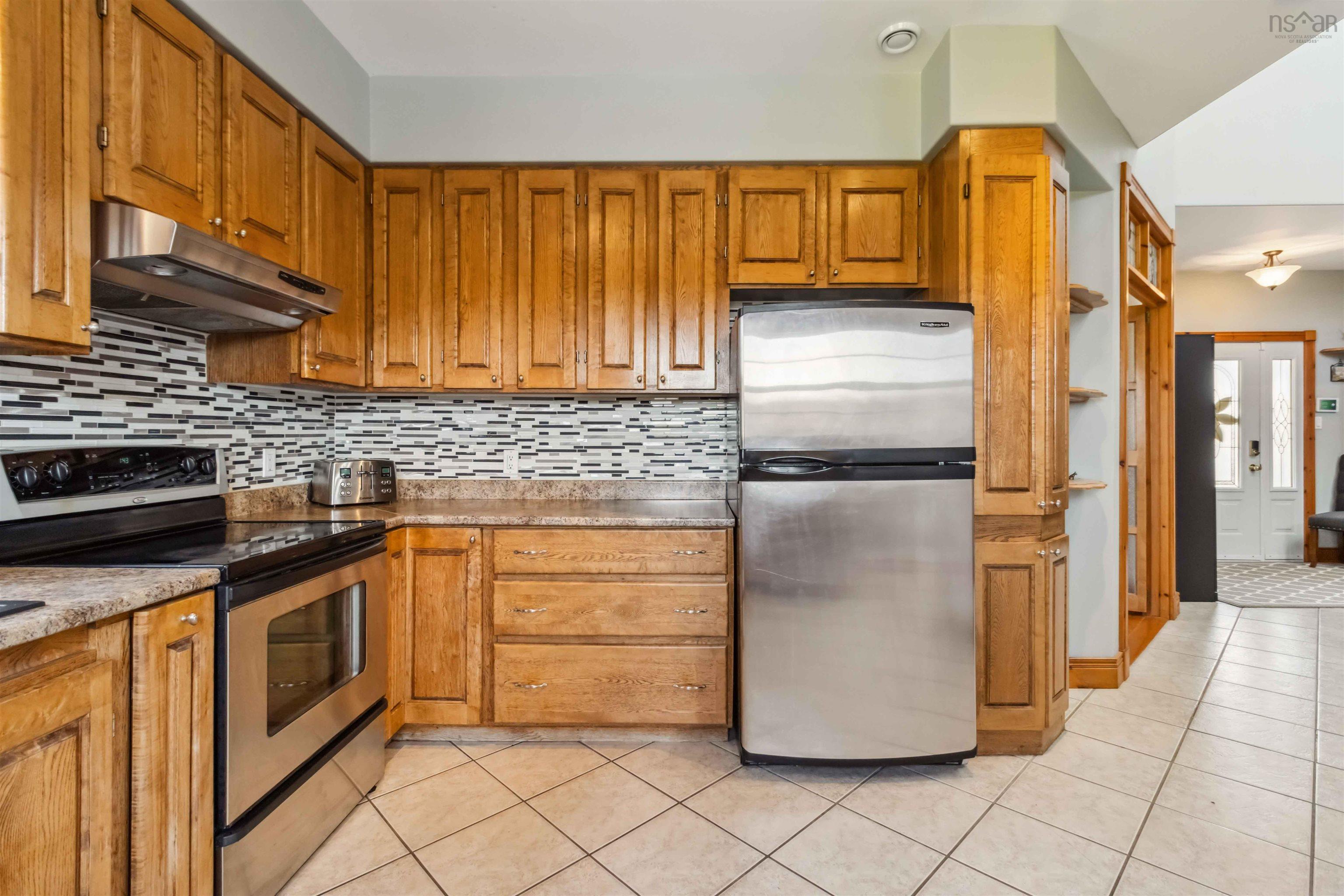Kitchen with appliances with stainless steel finishes, under cabinet range hood, light tile patterned floors, decorative backsplash, and brown cabinetry