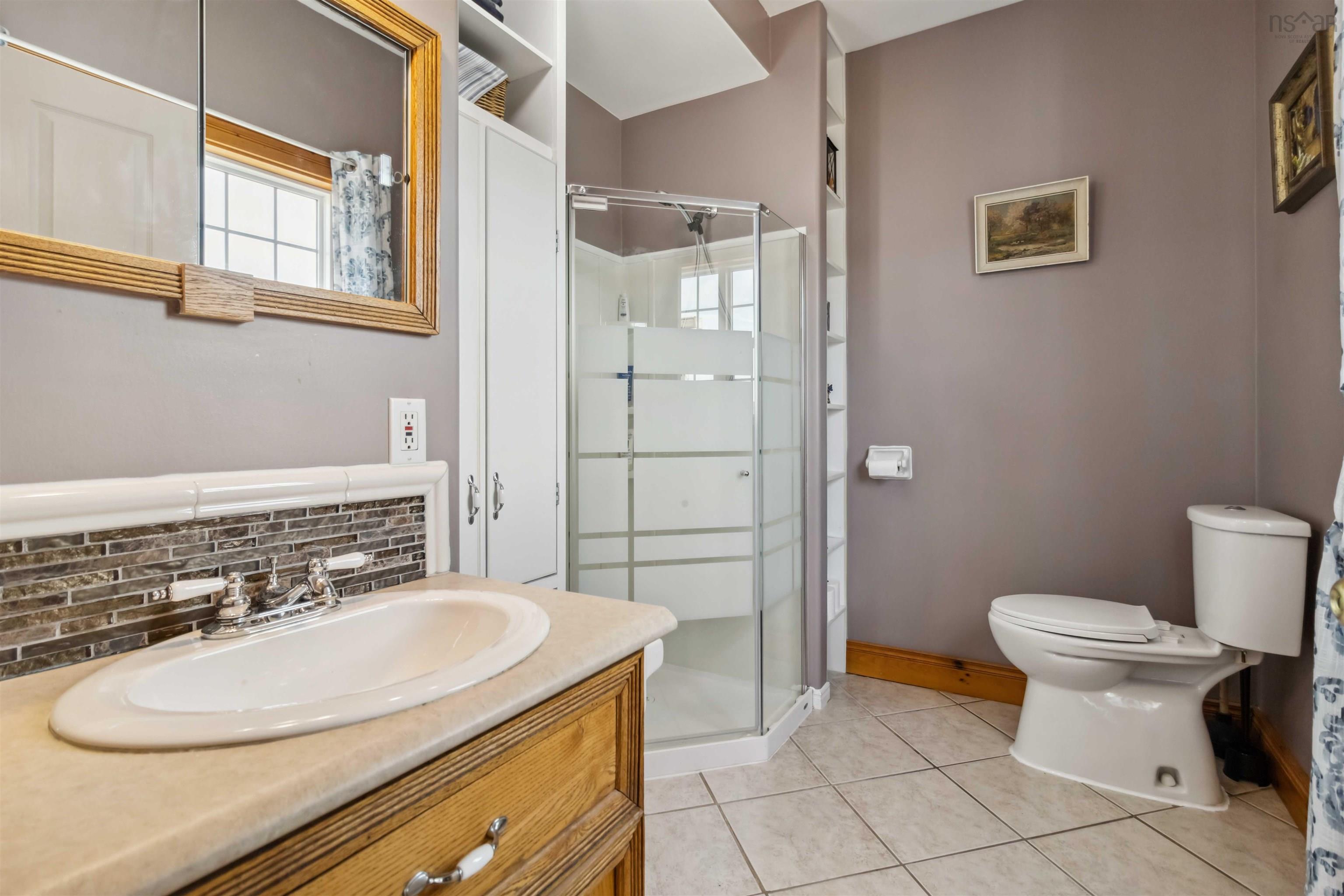 Bathroom with toilet, healthy amount of natural light, a shower stall, and backsplash