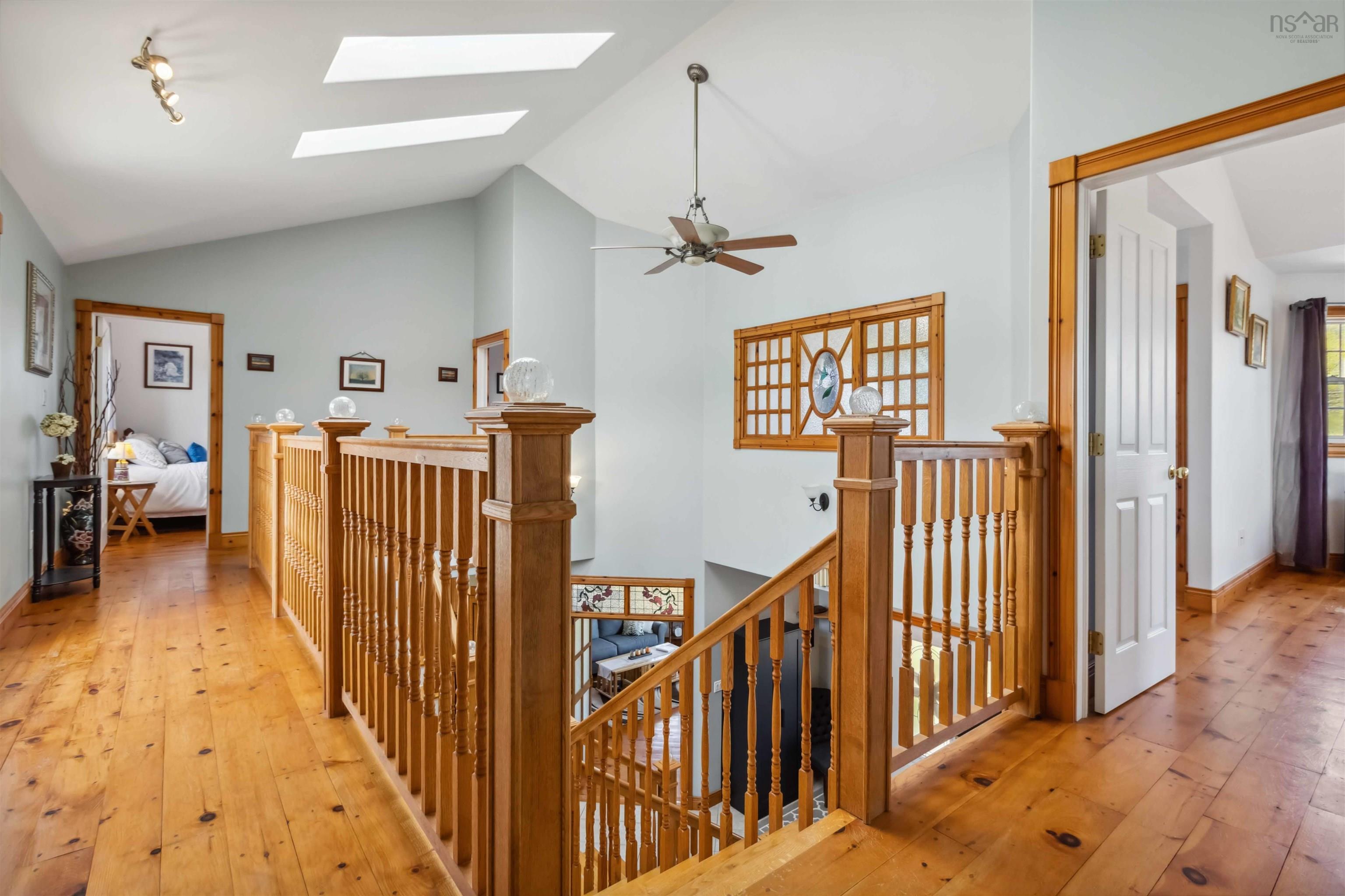 Corridor featuring an upstairs landing, vaulted ceiling, a skylight, and light wood finished floors