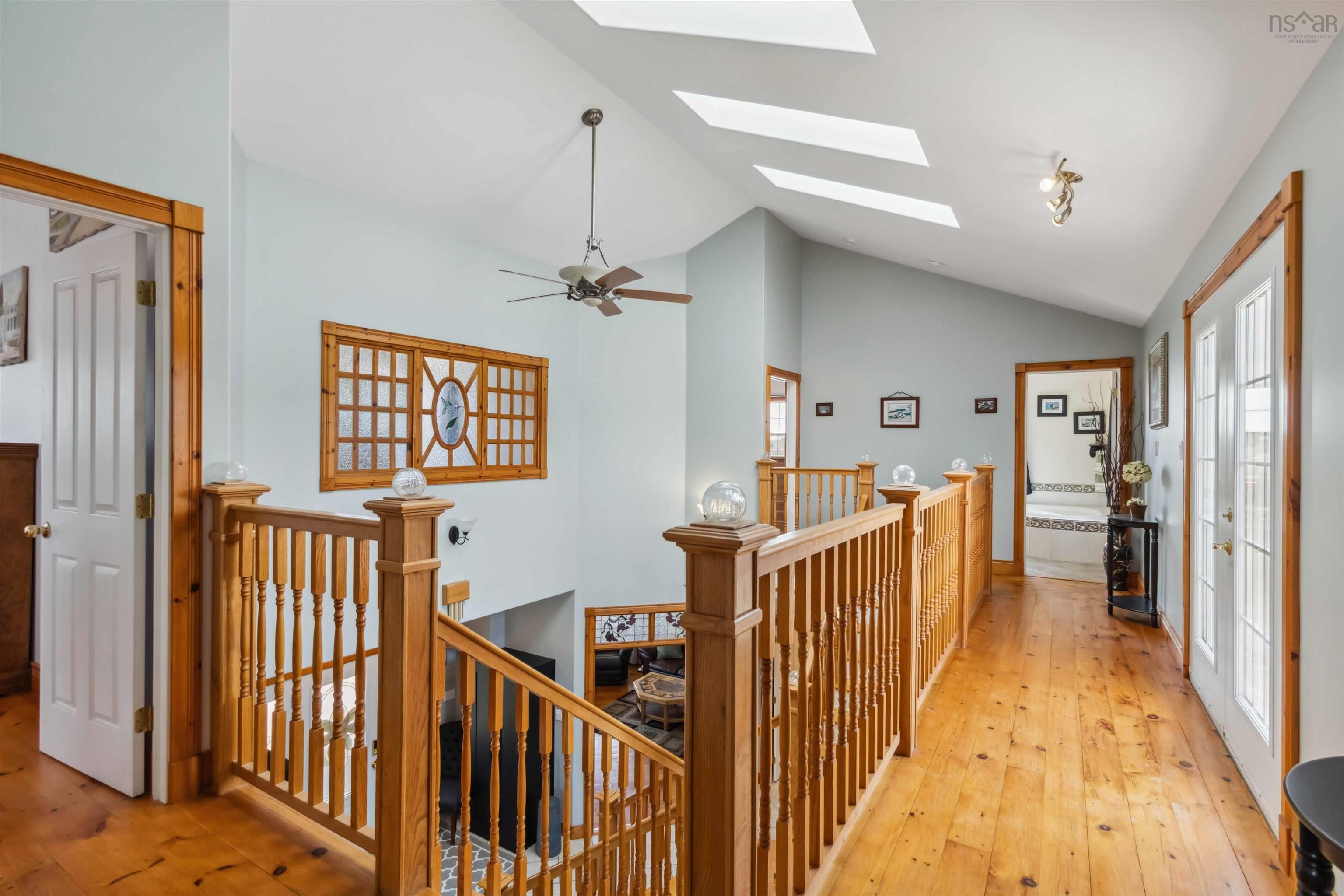 Corridor featuring an upstairs landing, lofted ceiling, a skylight, and light wood-style floors