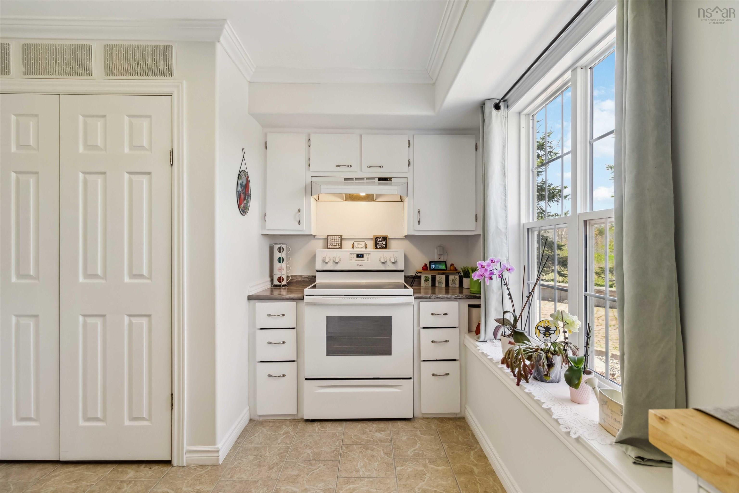 Kitchen with white electric range oven, under cabinet range hood, crown molding, white cabinets, and baseboards