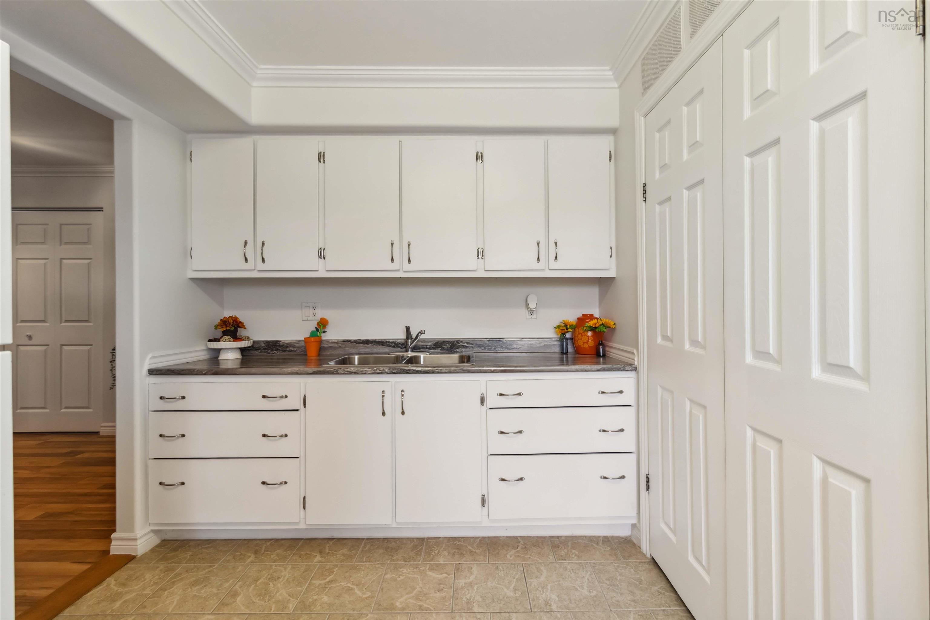 Kitchen featuring a sink, ornamental molding, white cabinetry, and dark countertops