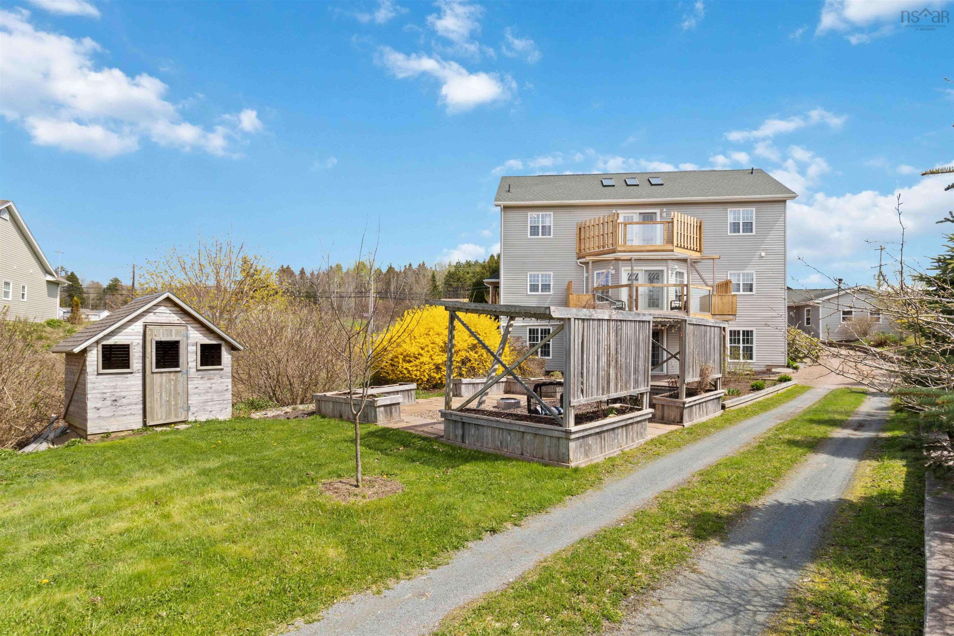 Back of property with a balcony, an outbuilding, a lawn, a storage unit, and driveway