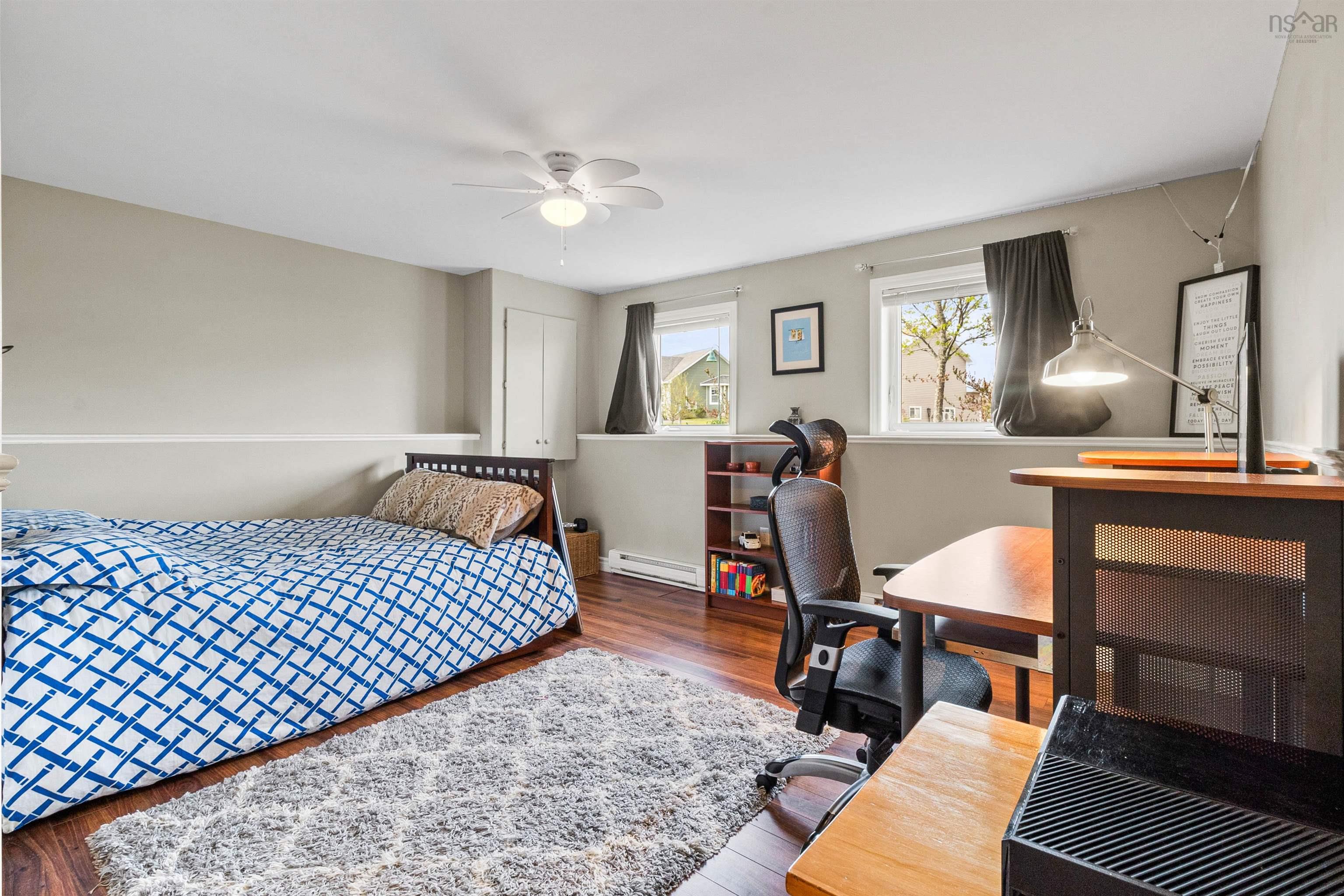 Bedroom featuring wood finished floors, a baseboard heating unit, an office area, and a ceiling fan