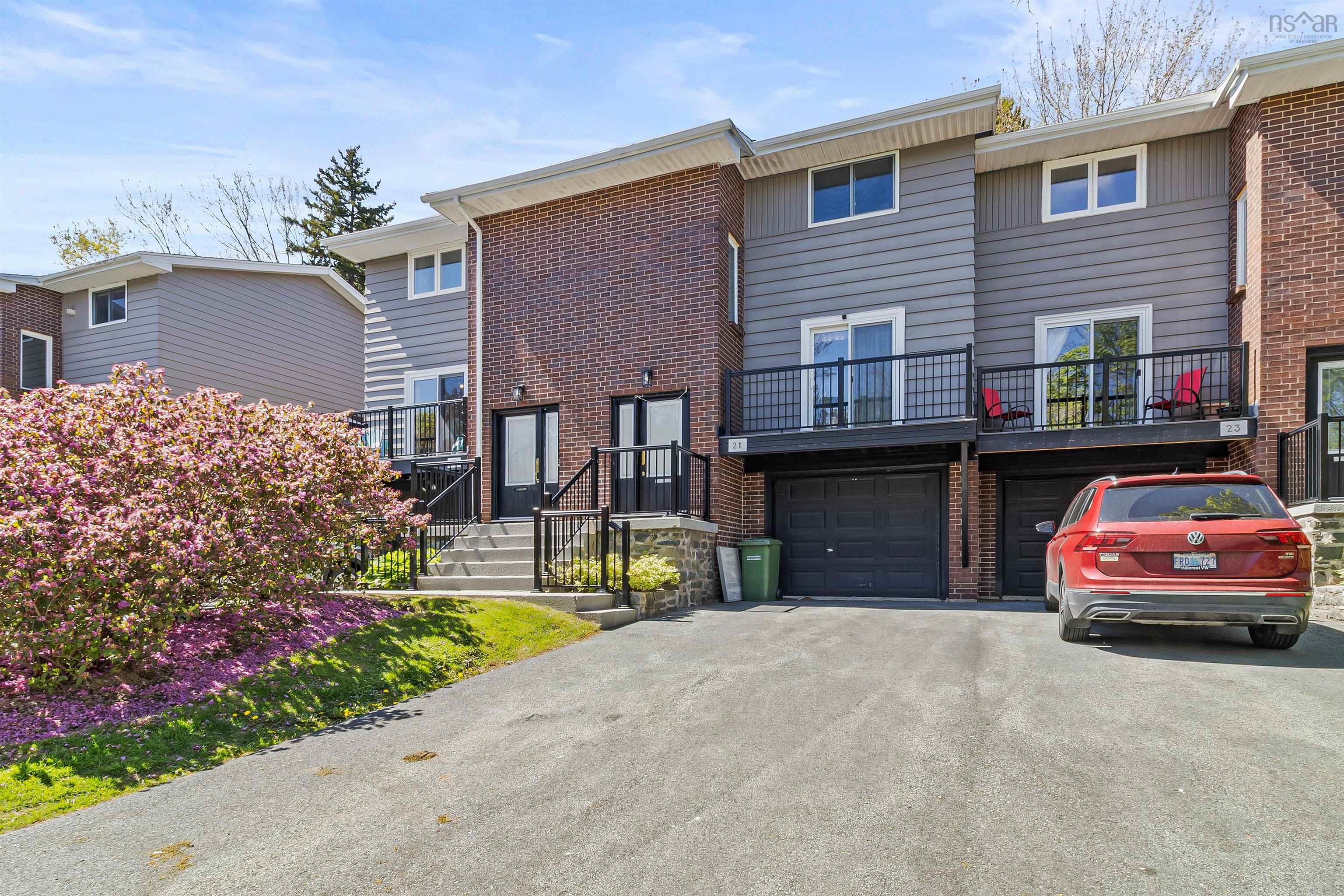Townhome property with driveway, an attached garage, brick siding, and a balcony