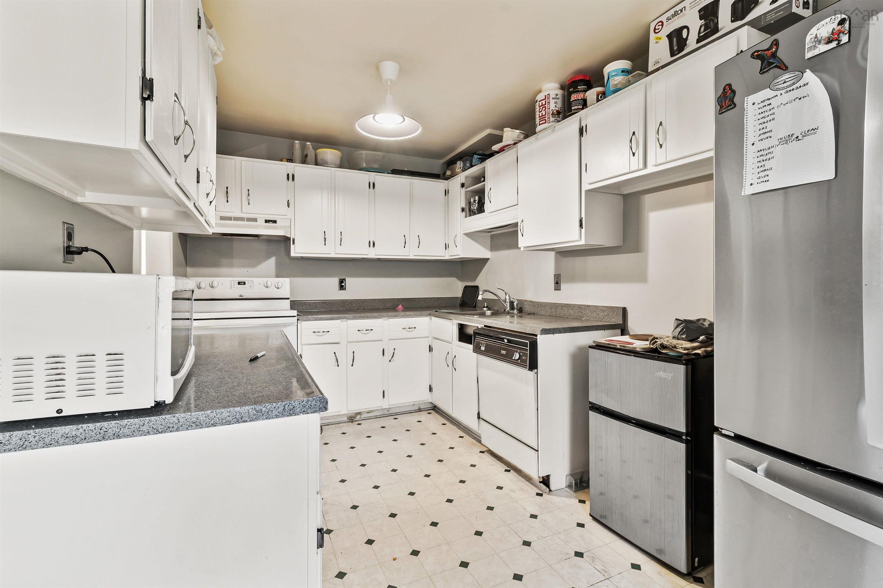 Kitchen featuring white appliances, under cabinet range hood, white cabinetry, and dark countertops
