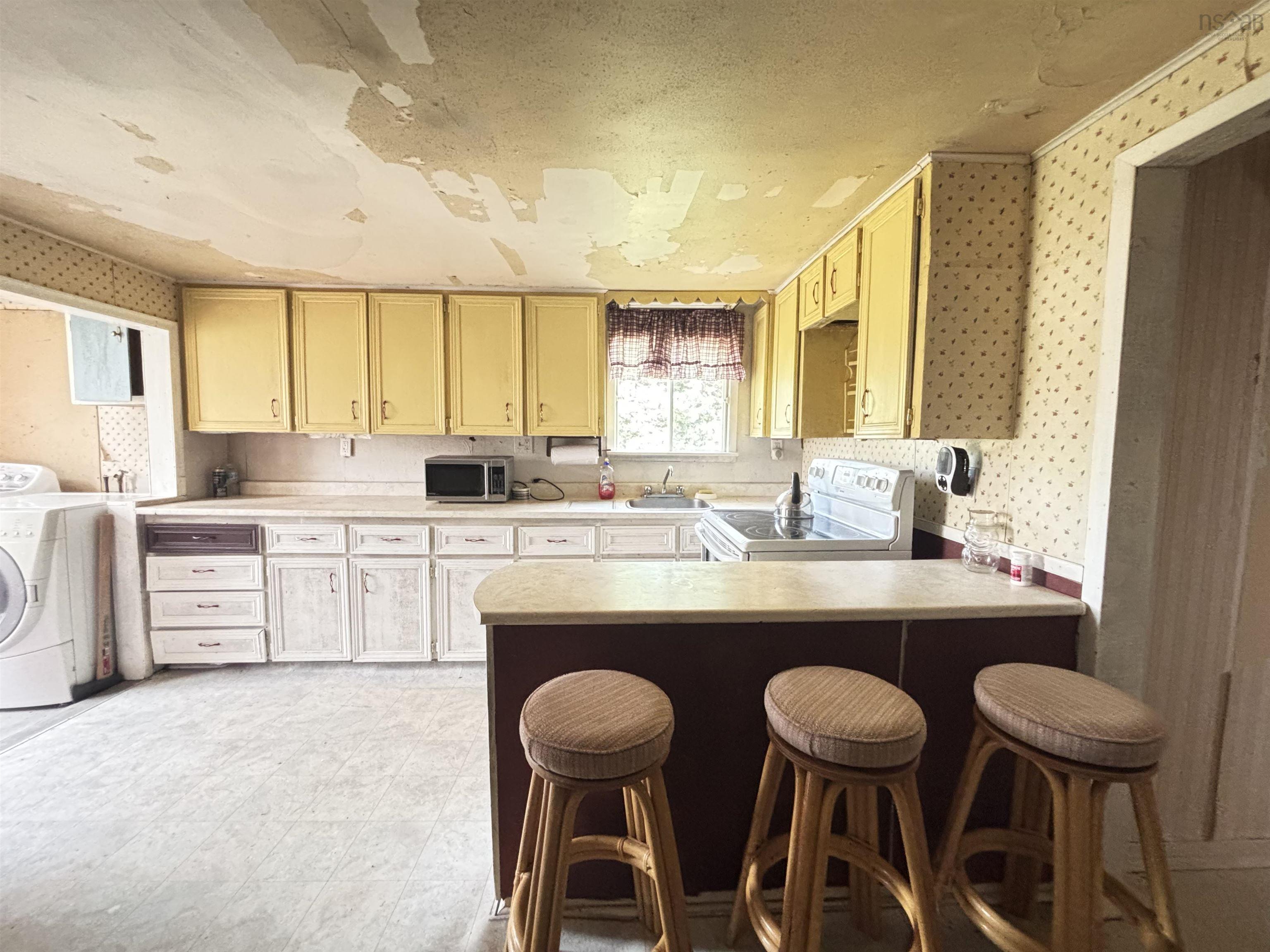 Kitchen with wallpapered walls, white electric range oven, light countertops, a peninsula, and a kitchen breakfast bar