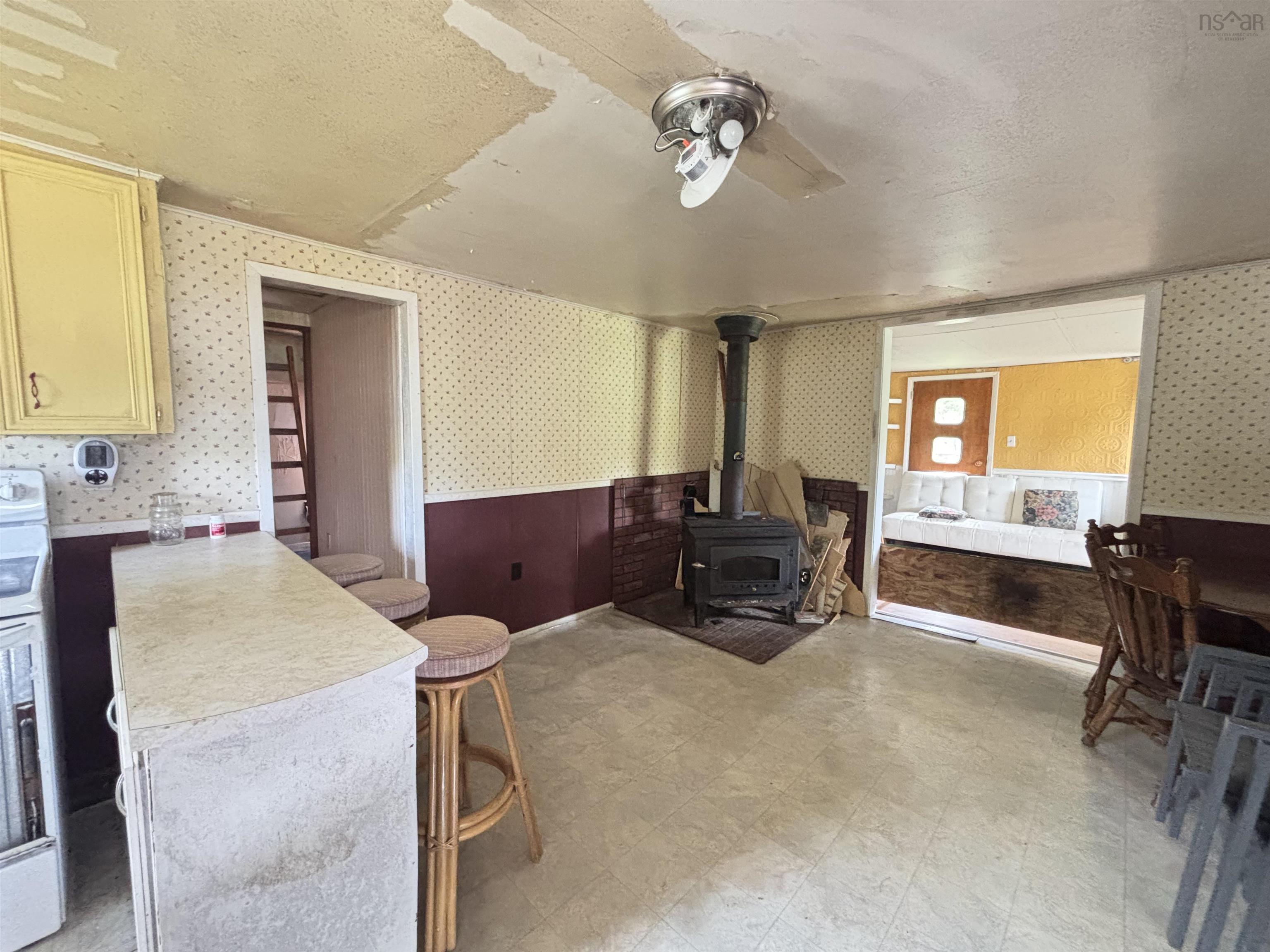 Living area with wallpapered walls, a wood stove, ceiling fan, wainscoting, and light floors