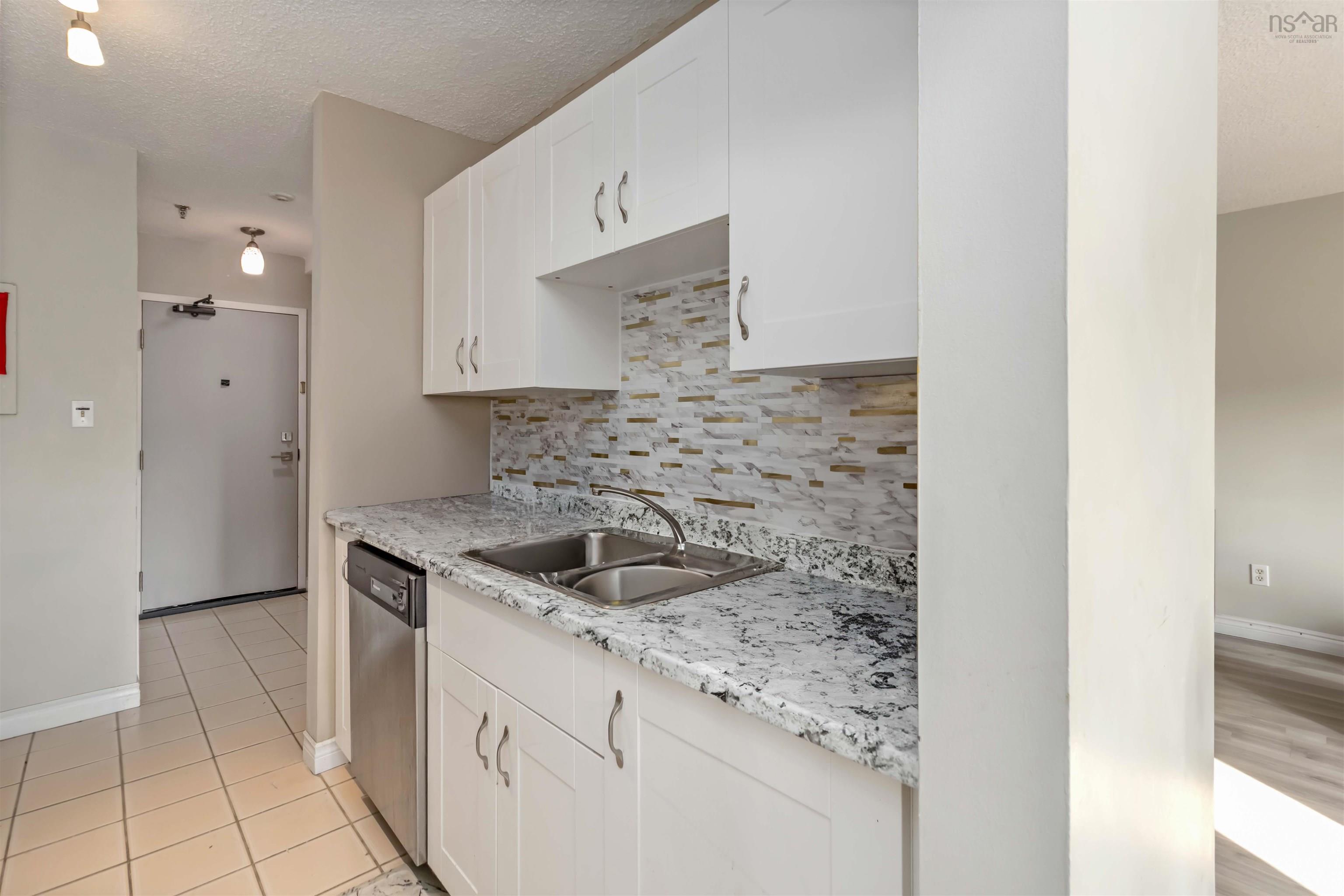 Kitchen featuring a textured ceiling, tasteful backsplash, white cabinetry, stainless steel dishwasher, and light stone countertops
