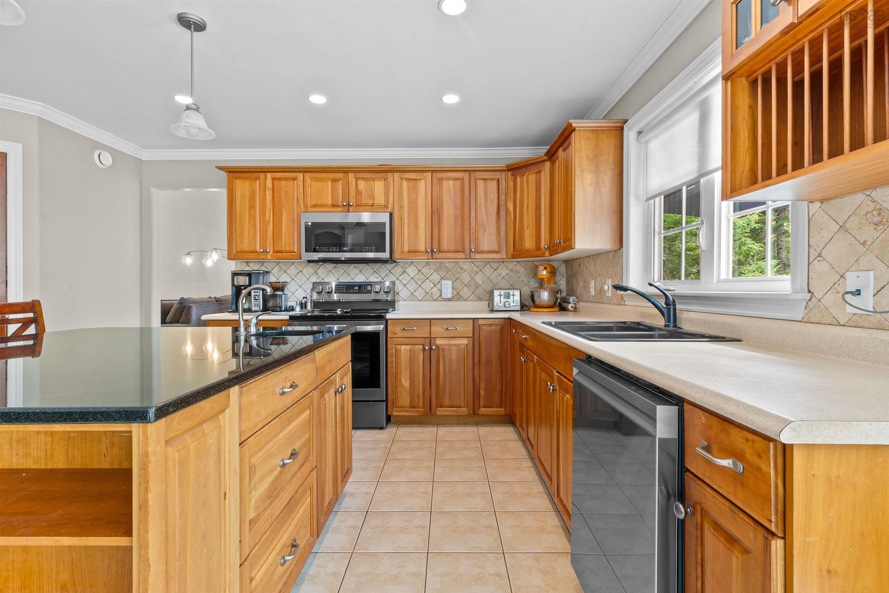 Kitchen featuring decorative backsplash, light tile patterned floors, crown molding, stainless steel appliances, and hanging light fixtures