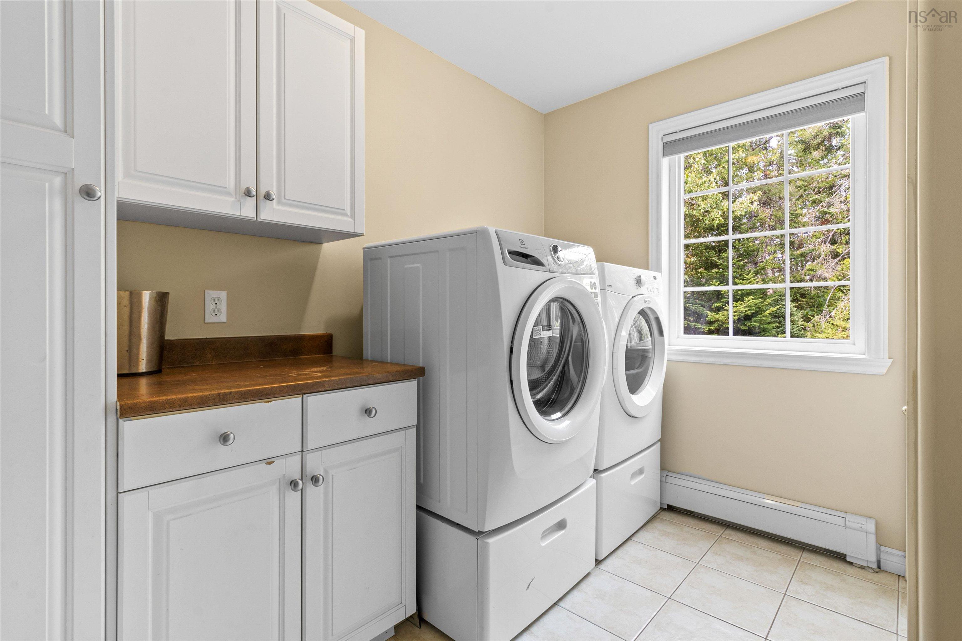 Washroom featuring a baseboard radiator, washing machine and clothes dryer, light tile patterned floors, and cabinet space