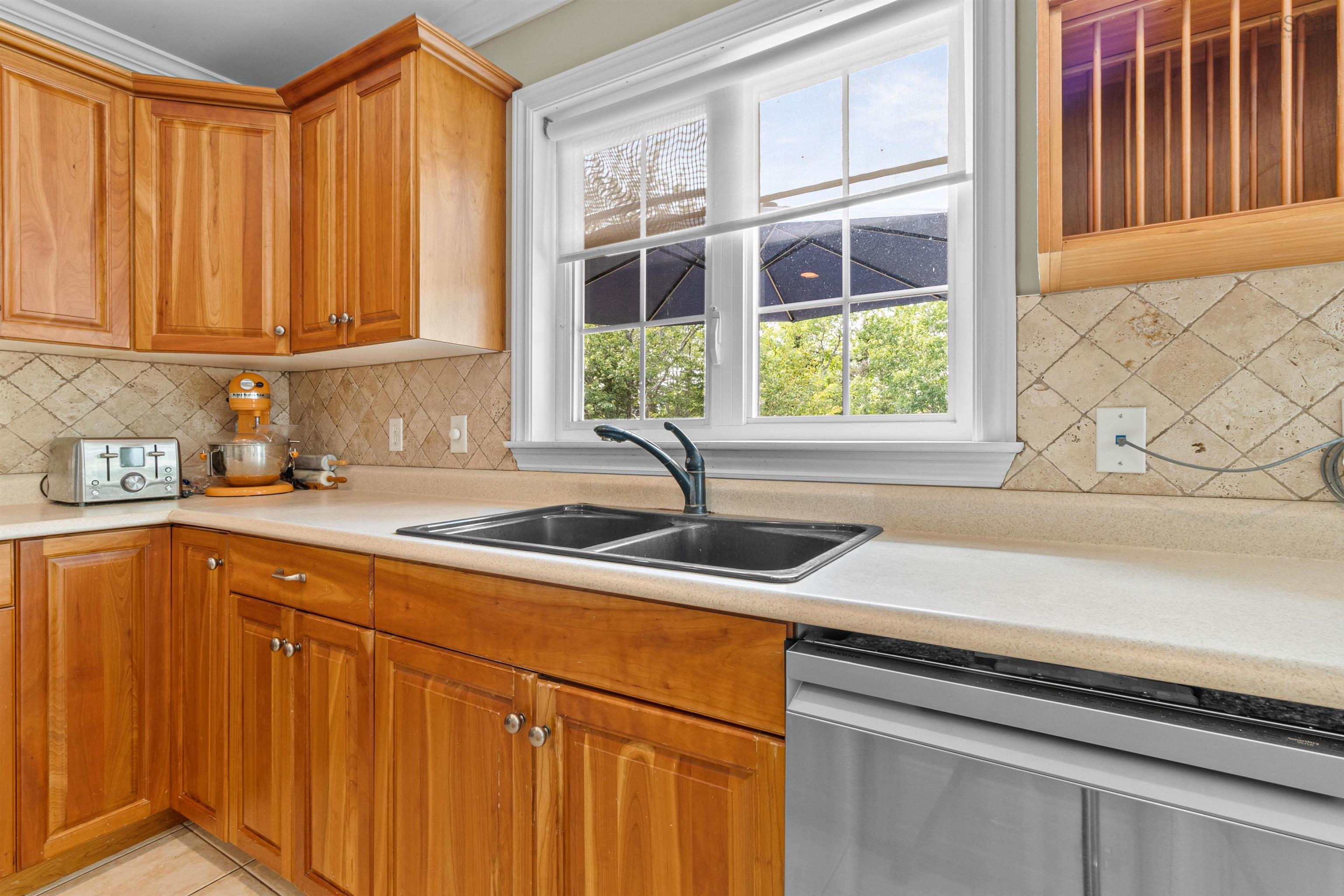 Kitchen with stainless steel dishwasher, backsplash, light countertops, and brown cabinetry
