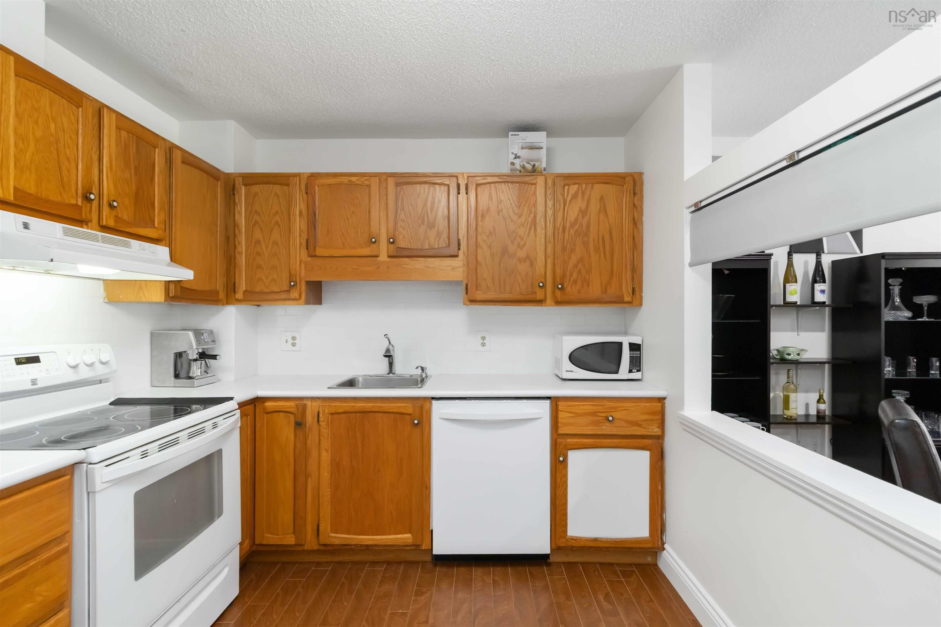 Kitchen with white appliances, dark wood-type flooring, light countertops, brown cabinetry, and under cabinet range hood