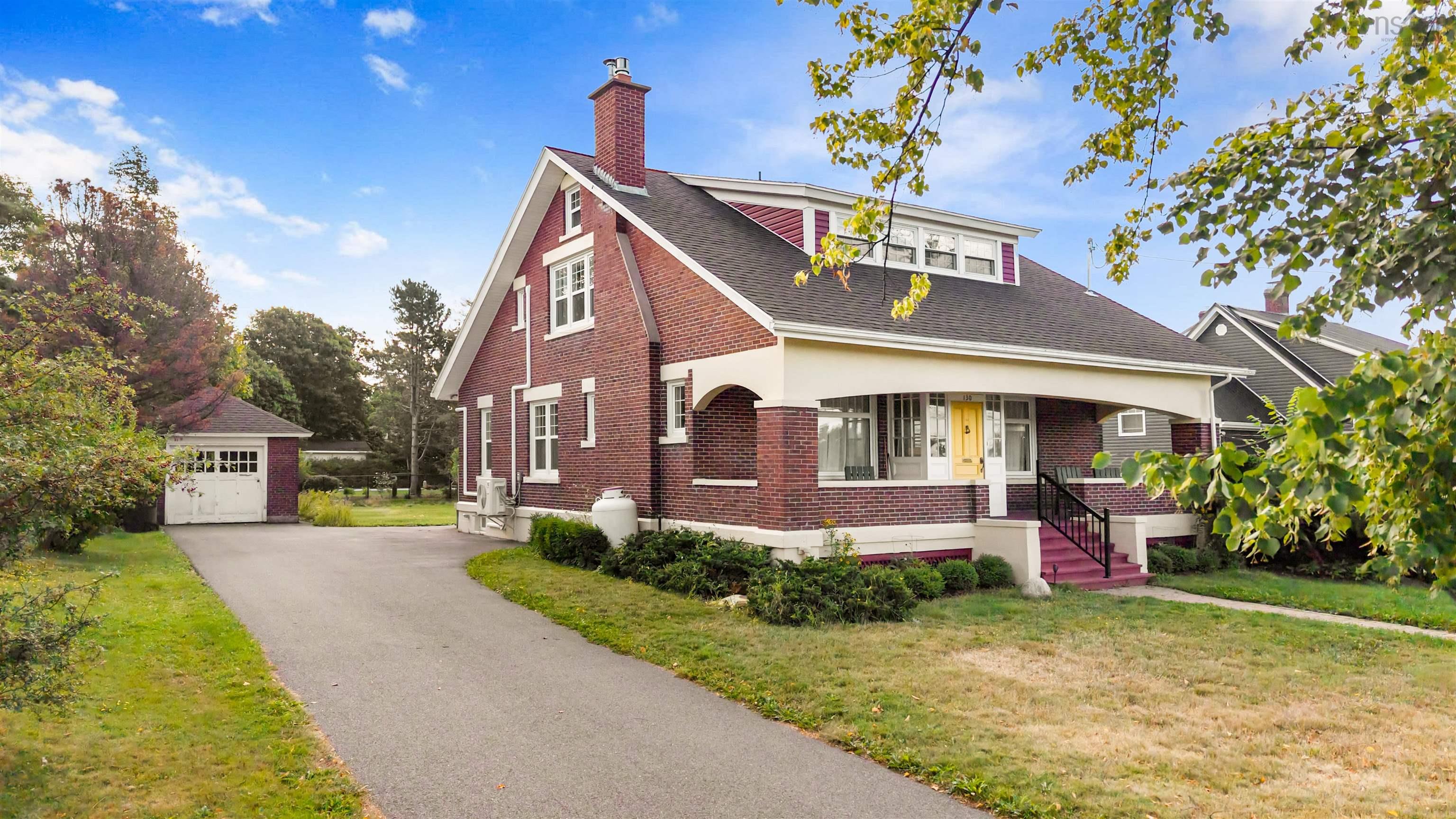 View of front of property featuring an outbuilding, brick siding, a chimney, a front yard, and covered porch