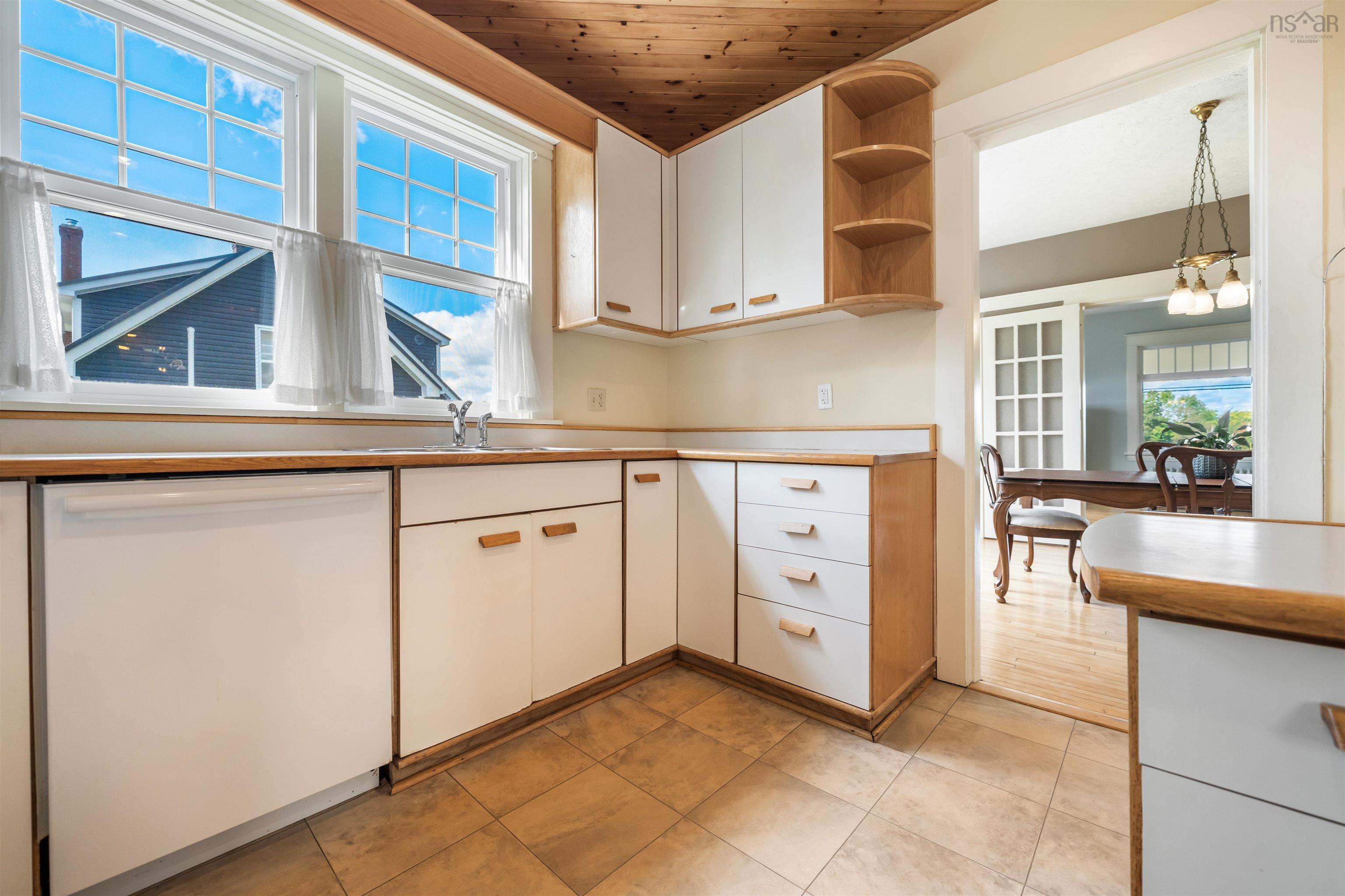 Kitchen with white dishwasher, white cabinetry, open shelves, light countertops, and hanging light fixtures