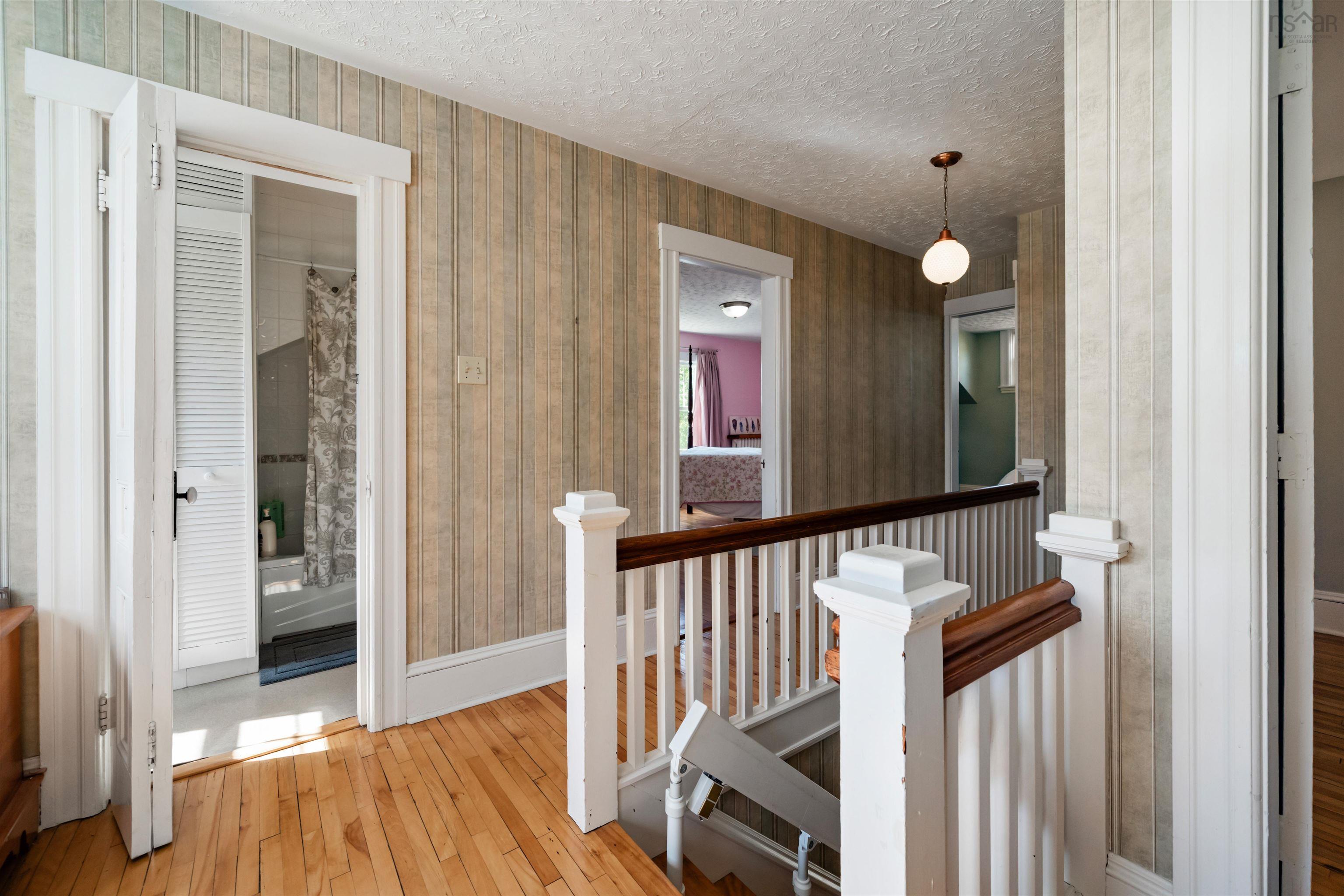 Hall with an upstairs landing, hardwood / wood-style floors, a textured ceiling, and wallpapered walls